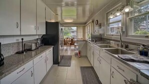 A modern kitchen with white cabinets, granite countertops, and stainless steel appliances. There is a dining area visible through an open door. - LOOK!  Spacious Home in the Heart of Hilo - Bonus Rec Room! (Hilo)