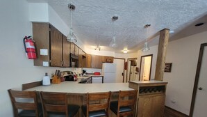 Eine kompakte Küche mit Holzausstattung, einer zentralen Kochinsel mit Barhocker, einer Mikrowelle und einem Kühlschrank.