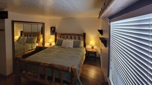 Ein Schlafzimmer mit einem hölzernen Bett, einem Spiegel, Nachttischlampen und einem Fenster mit Jalousien.