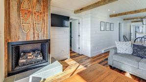 A living room with a fireplace, wooden flooring, a gray sofa, and a TV mounted on the wall.