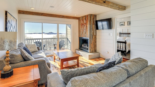 A spacious living room with a fireplace, large windows, and a view of the mountains.