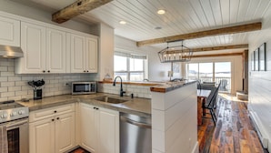 A modern kitchen with white cabinets, a stainless steel sink, and a wooden ceiling beam.