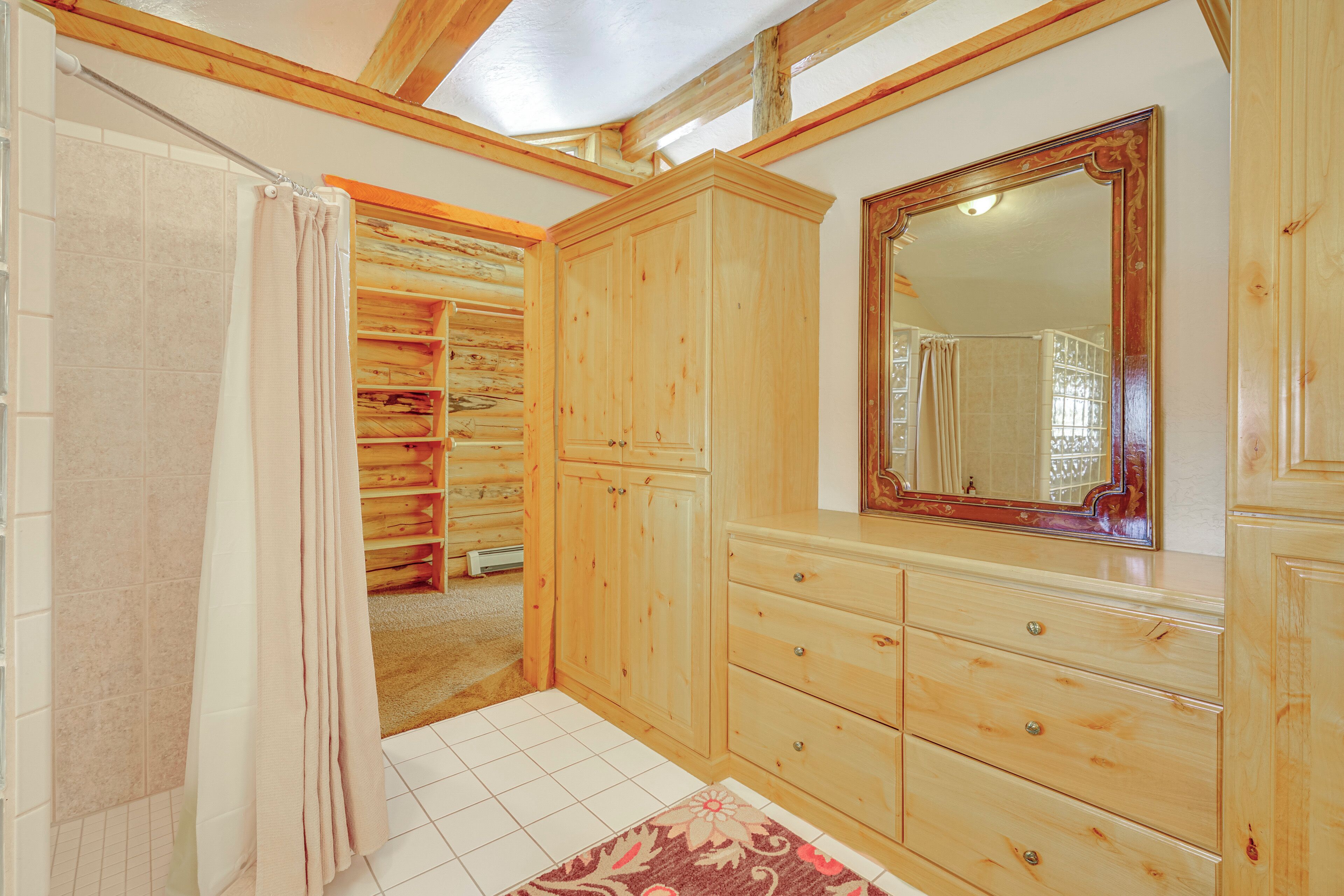 A wooden bathroom with a large mirror, a shower curtain, and a tiled floor.