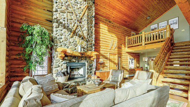 A log cabin interior with a stone fireplace, wooden furniture, and a balcony.