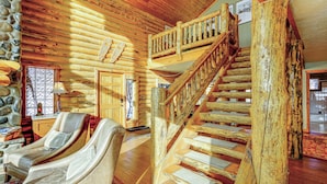 A log cabin interior with a wooden staircase, a lounge area with recliners, and a stone wall.