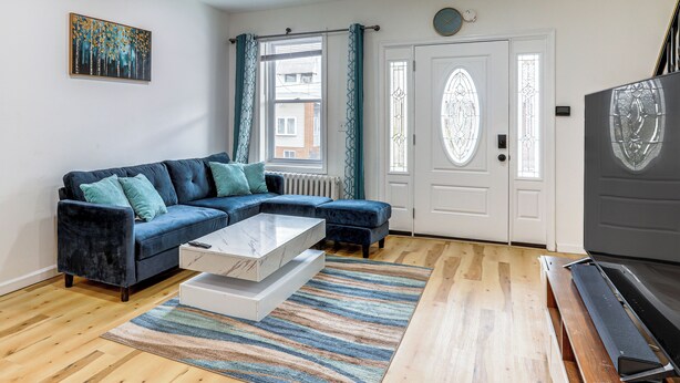 A living room with a sectional sofa, a coffee table, a flat-screen TV, and a large window with curtains. - 6 Mi to Eagles Games: Stylish Philly Townhome! (Philadelphia)