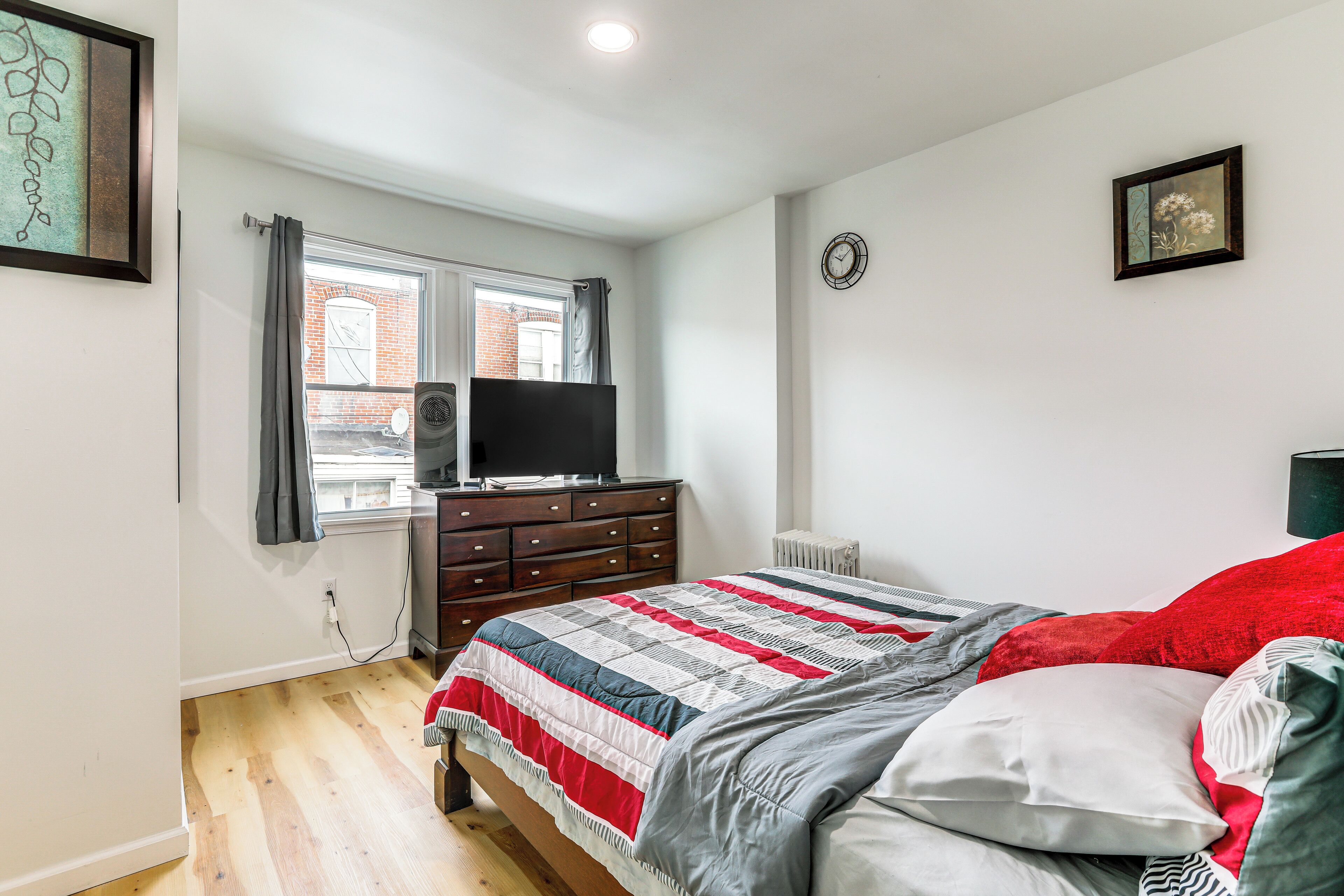A bedroom with a bed, a dresser, a television, a window with curtains, and a radiator.