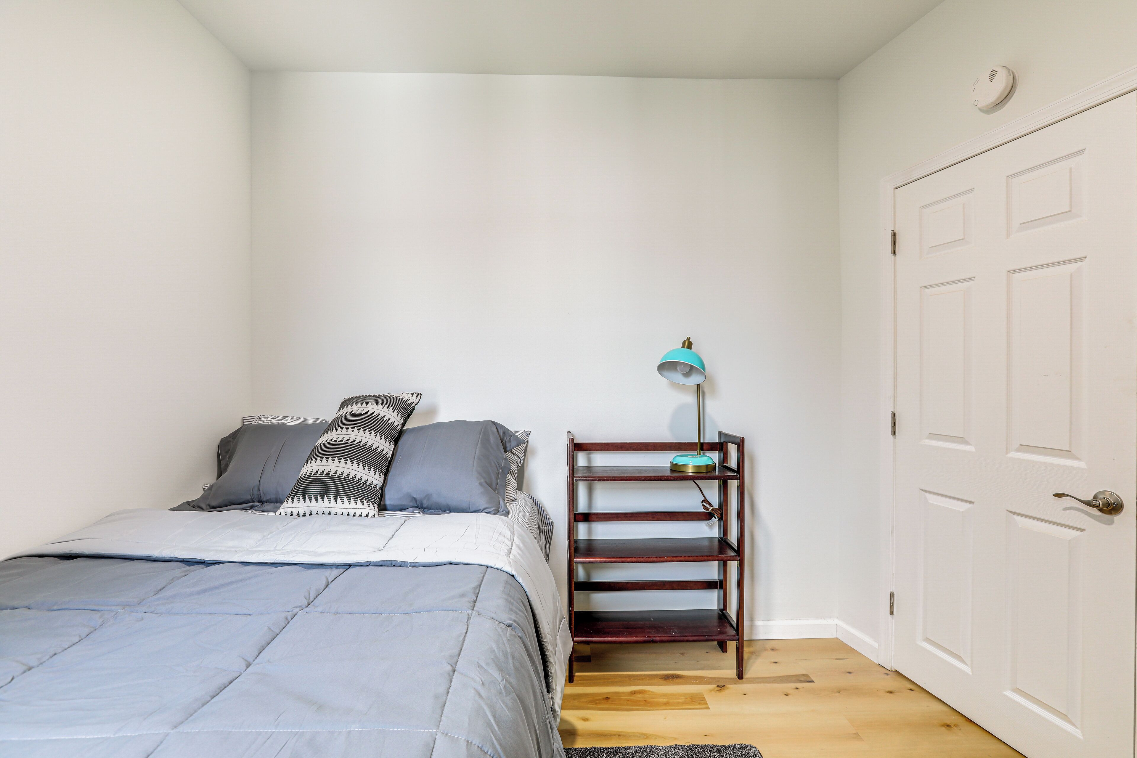 Una camera da letto con un letto, un comodino con una lampada, una porta e una parete bianca.