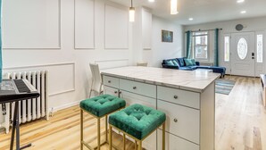A modern kitchen with a marble countertop, two green bar stools, a white radiator, and a blue sofa in the background. - 6 Mi to Eagles Games: Stylish Philly Townhome! (Philadelphia)