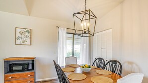 A dining area with a wooden table, chairs, a white bowl with fruit, a microwave in a wooden cabinet, and a geometric pendant light. - Bring Your Pup: Spring Valley Home w/ Fenced Yard! (Mayer)