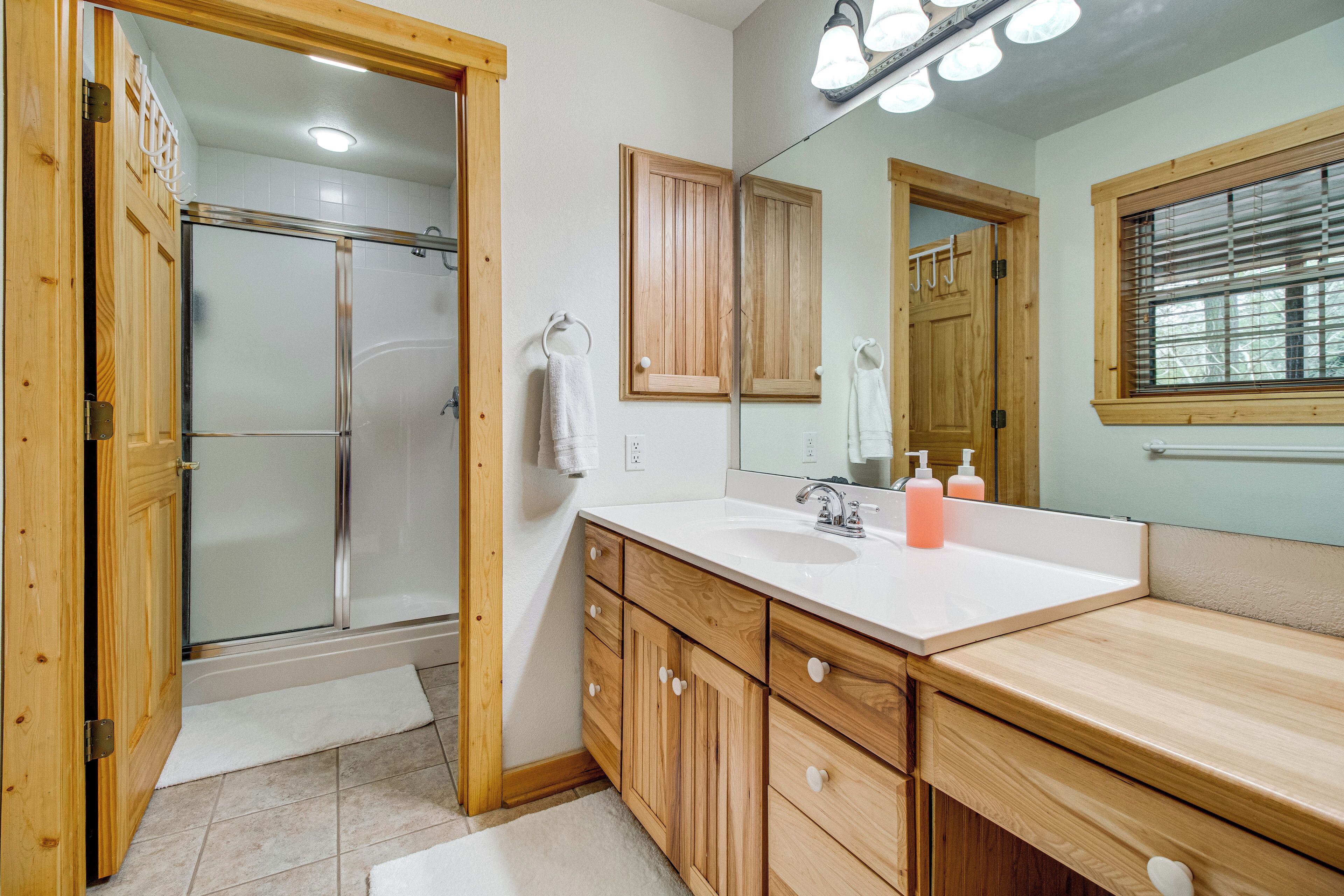 A bathroom with a shower, wooden cabinets, a sink, and a mirror.