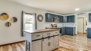 A kitchen with a central island, dark blue cabinets, a microwave, and a sign that says "gather". - 17 Mi to Brookville Lake: Home w/ In-unit Laundry (Connersville)