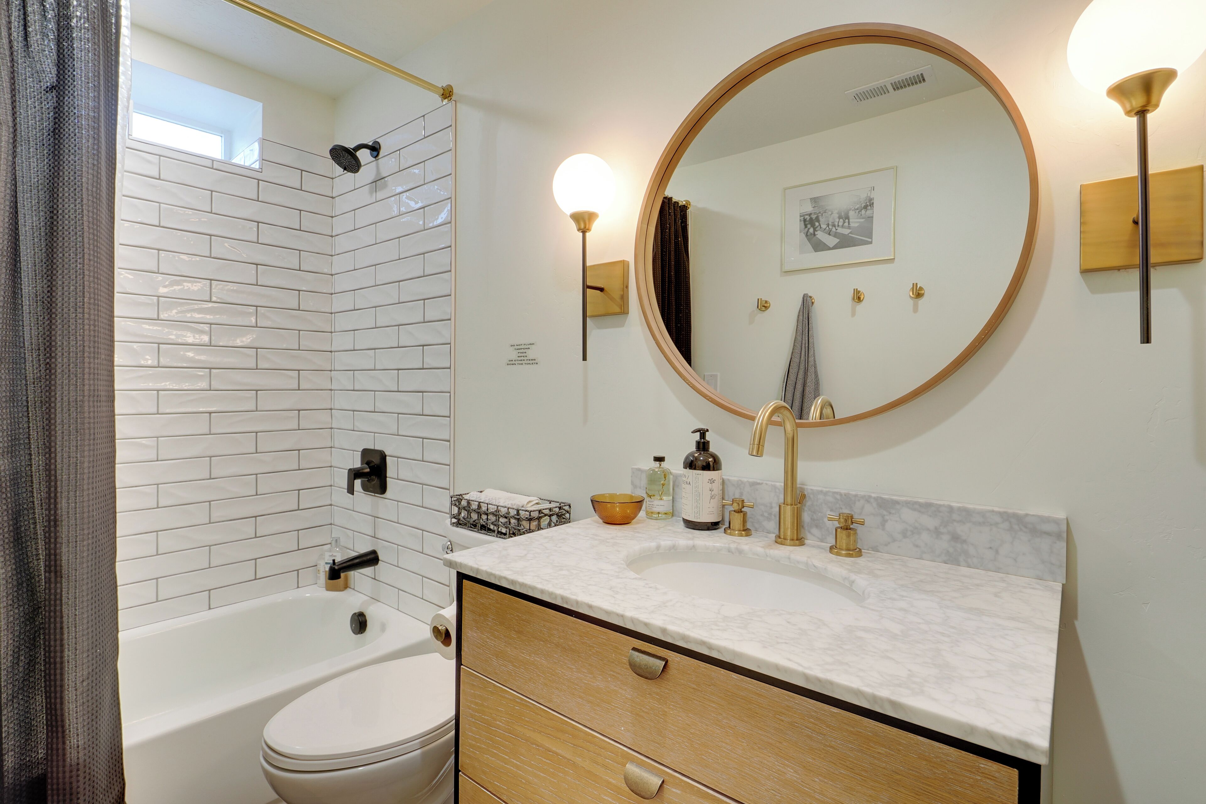 A modern bathroom with a white tiled shower, a white bathtub, a marble sink, and a wooden vanity.