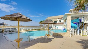 A pool area with umbrellas, a slide, and a building with a pool entrance. - Walk to Whitecap Beach: Corpus Christi Retreat (Corpus Christi)