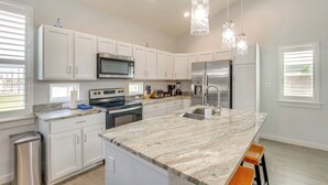 A modern kitchen with white cabinets, stainless steel appliances, a marble countertop, and pendant lighting. - Walk to Whitecap Beach: Corpus Christi Retreat (Corpus Christi)