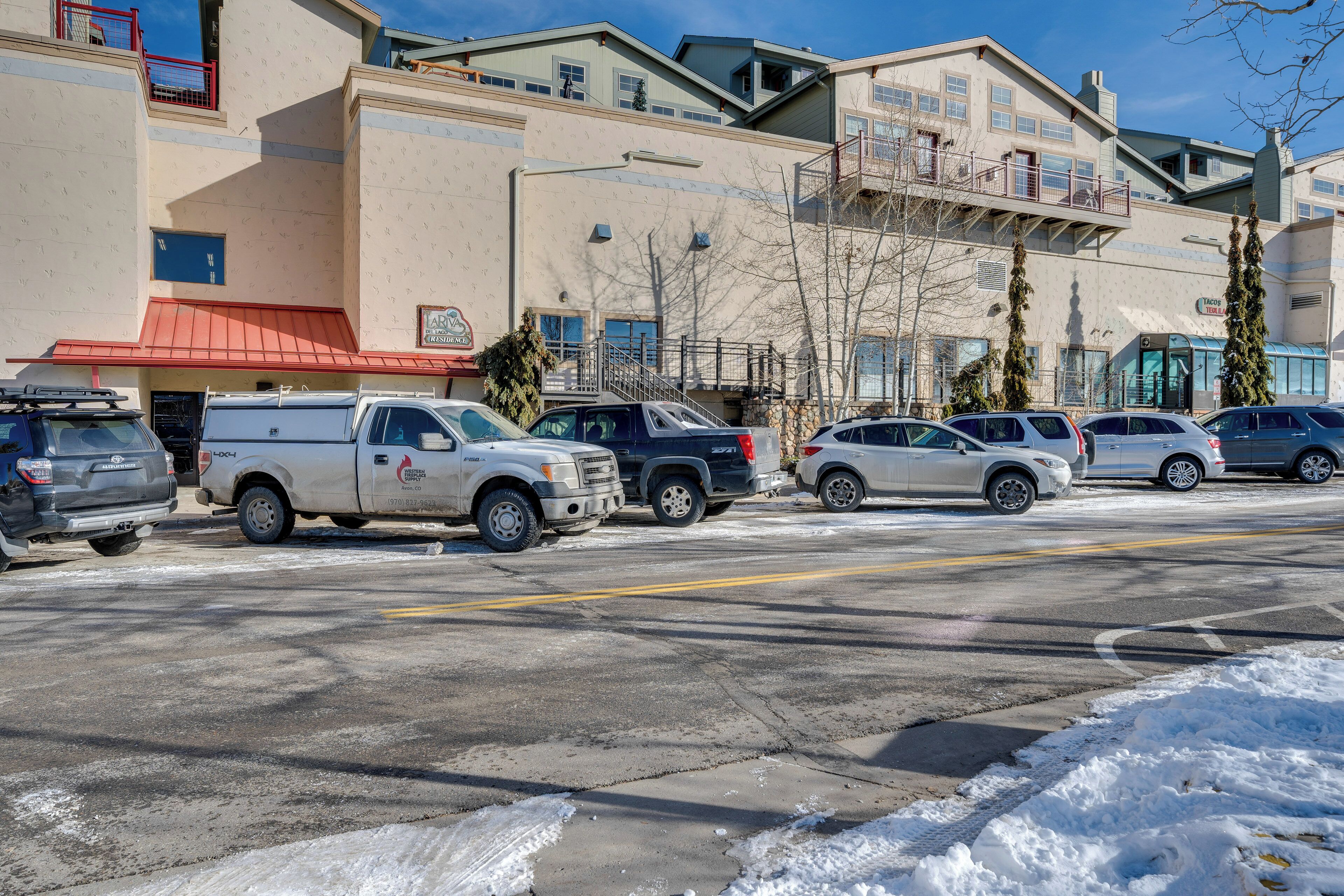 A parking lot with several vehicles, including a white truck and SUVs, in front of a building with a red awning and a sign that reads "Taco Bell."
