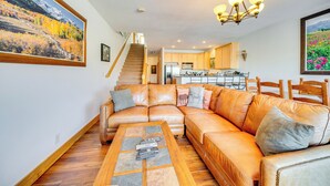 Ein Wohnzimmer mit einem ledernen Ecksofa, einem Couchtisch mit Fernbedienungen und einer Treppe, die zur Küche führt.