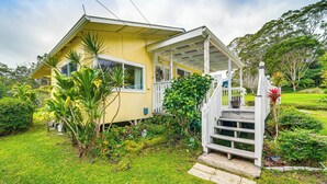 Ein gelbes Haus mit einer Veranda, umgeben von üppigem Grün und einem gepflegten Rasen.