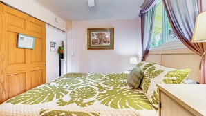 Ein Schlafzimmer mit Bett, einem Holzschrank, einem gerahmten Bild an der Wand und einem Fenster mit Vorhängen.
