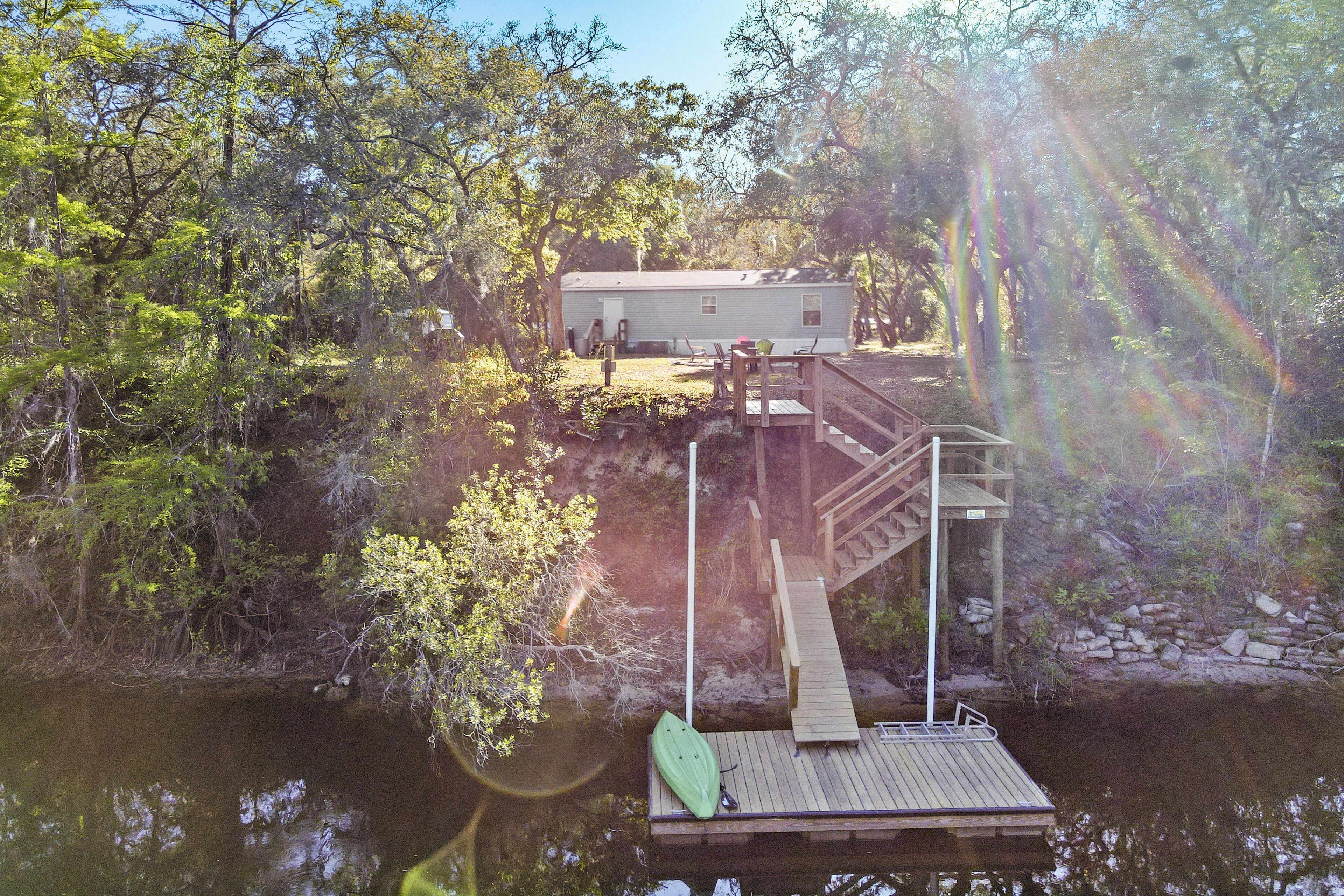 A house on a cliff by a lake with a dock and a green kayak.