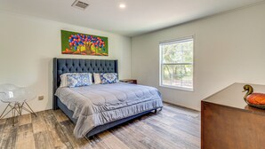 A bedroom with a large bed, a window, and a painting on the wall.