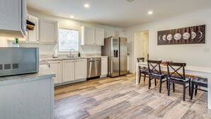 A modern kitchen with white cabinets, a stainless steel refrigerator, and a dining area with dark wooden chairs.