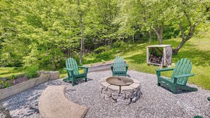 Een terras met Adirondack-stoelen, een vuurkorf van steen en een houten bank.