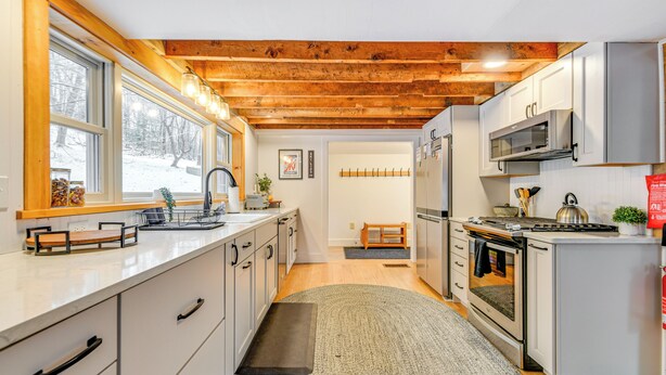 Een moderne keuken met witte kasten, een houten plafond en een groot raam.