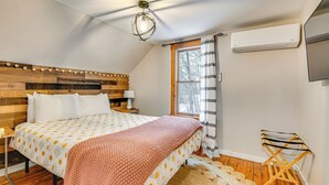 Een slaapkamer met een houten hoofdbord, een bed met beddengoed met een patroon, een bedlampje, een raam met gordijnen en een houten vloer.