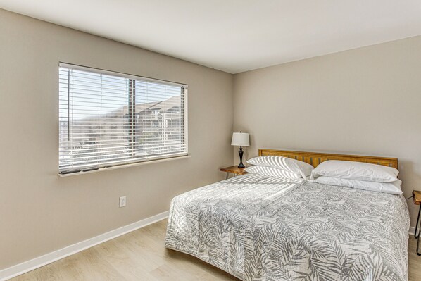 A bedroom with a large bed, a nightstand, a lamp, and a window with blinds.