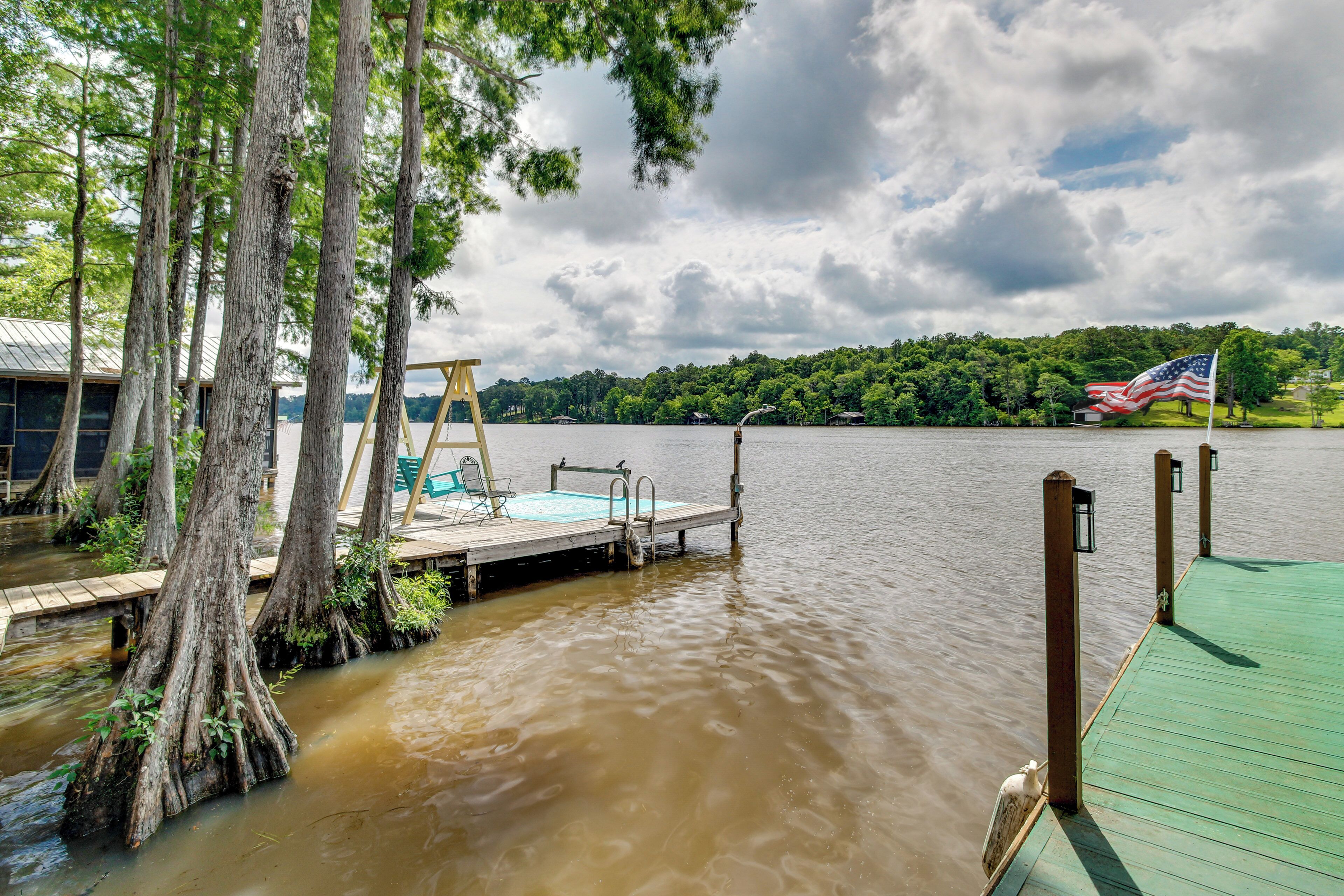 Une jetée s’avançant dans un lac aux eaux troubles, avec une plateforme en bois et une chaise suspendue, le tout entouré d’arbres.