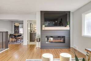 Una sala de estar moderna con chimenea, piso de madera y una zona de comedor con mesa y sillas.
