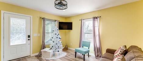 A living room with a white Christmas tree, a grey sofa, and a television mounted on the wall.