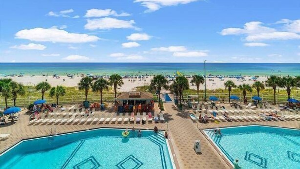 Un área de piscina con dos piscinas, una playa al fondo y palmeras bordeando la piscina.