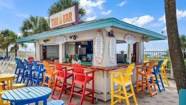 Eine Strandbar mit bunten Stühlen und Tischen, einer Speisekarte und einem Schild mit der Aufschrift 'The Bar'.