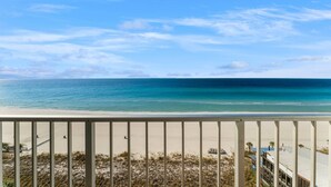Vista a la playa desde un balcón con barandilla, playa de arena y océano.