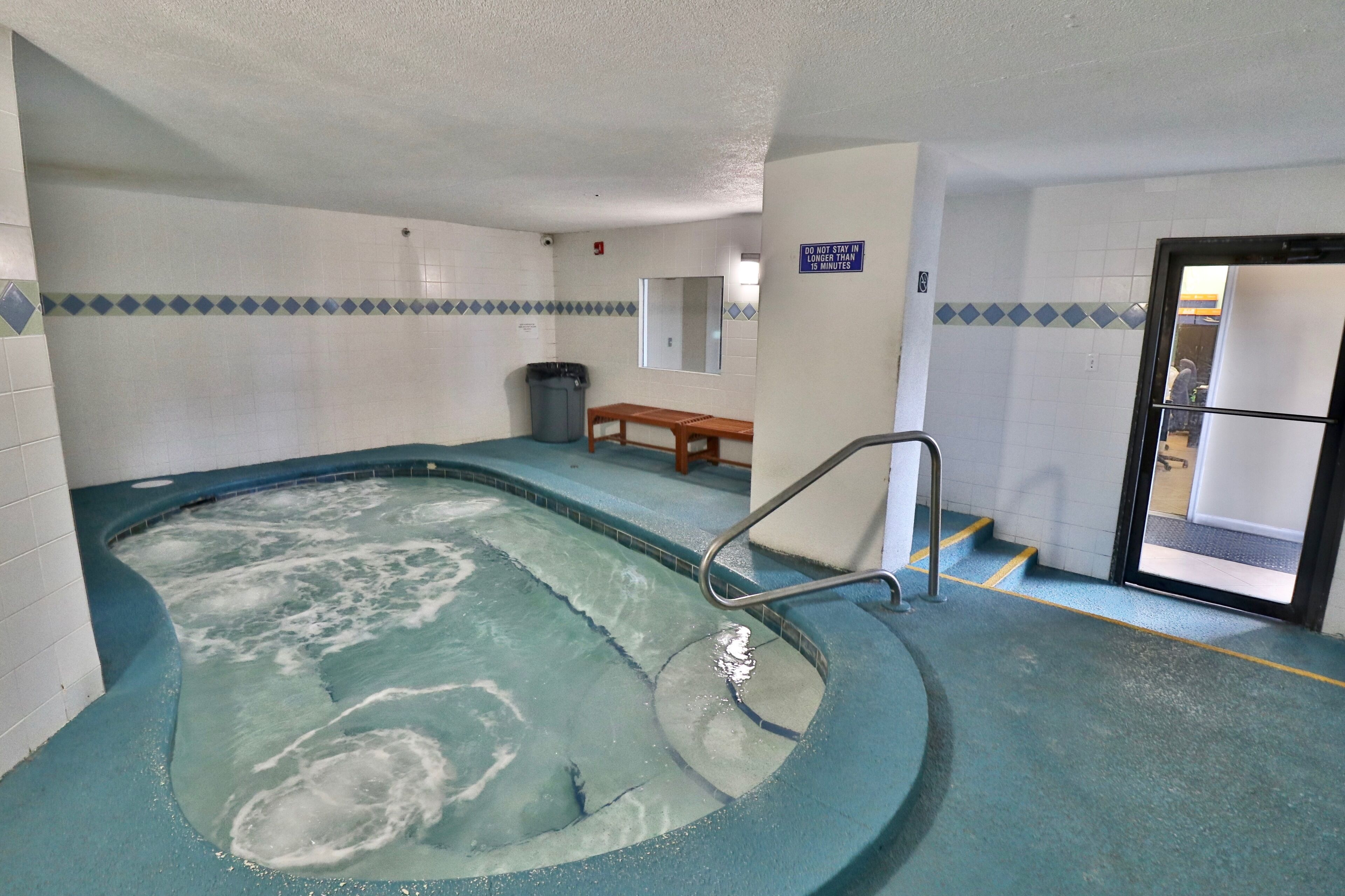 Un espace détente avec un jacuzzi, un banc en bois et une poubelle.
