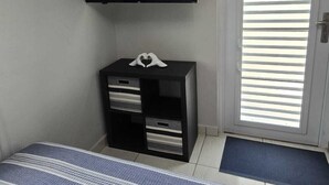 Ein Zimmer mit einem Bett, einem an der Wand befestigten Fernseher, einem kleinen schwarzen Schrank und einer Tür mit Jalousien.