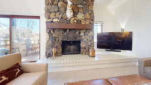 Un salón con chimenea de piedra, televisión de pantalla plana y vistas al exterior.