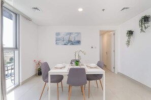 Un comedor con una mesa blanca, cuatro sillas grises y un cuadro de veleros en la pared.
