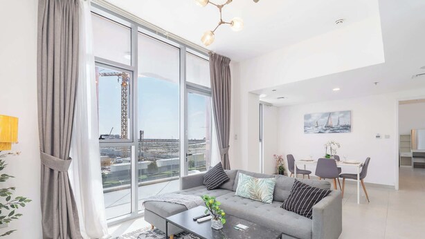 Un salon moderne avec un canapé gris, une table basse et une vue sur un chantier de construction, visible à travers de grandes fenêtres.