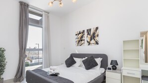 Une chambre moderne avec un grand lit, une vue sur la ville par la fenêtre et un décor minimaliste.