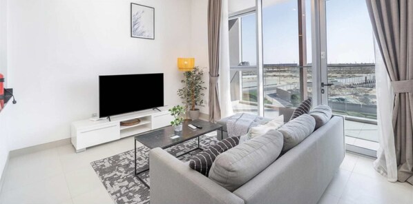 Una sala de estar moderna con una televisión de pantalla plana, un sofá, una mesa de centro y un ventanal con vistas a un puente.