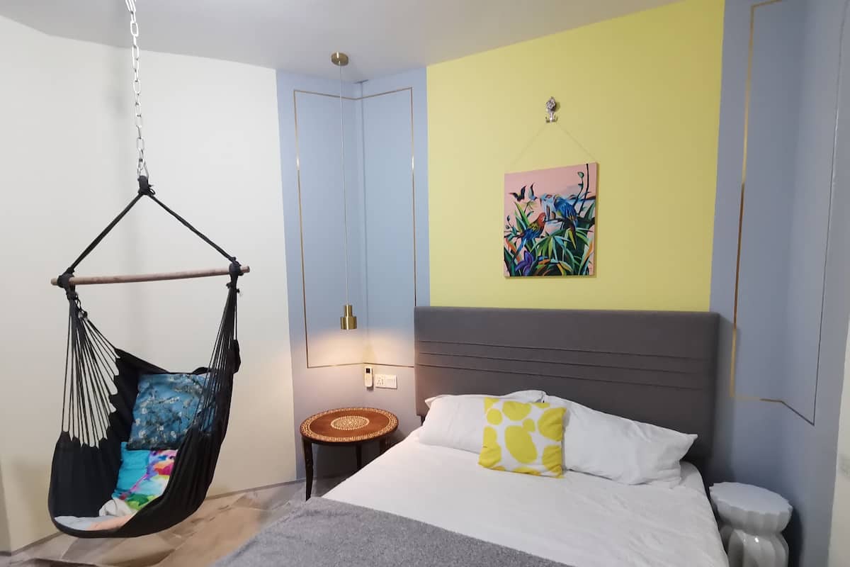 Ein Schlafzimmer mit Bett, Hängesessel, Nachttisch und Wandbild.