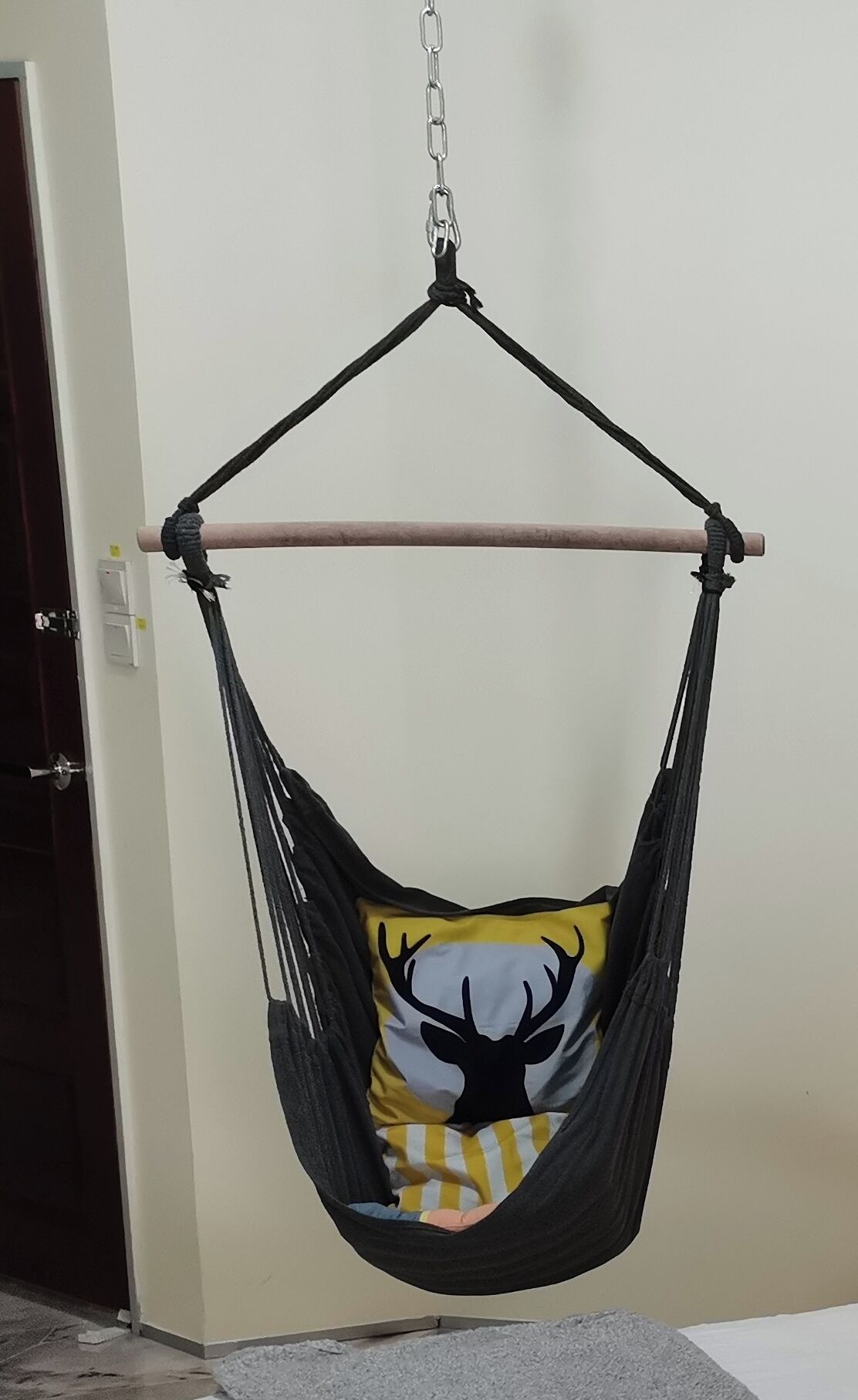 A black hammock chair with a cushion featuring a deer design, suspended by a chain from a ceiling hook.