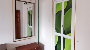 A room with a wooden dresser, a mirror, an air conditioning unit, and a door with green abstract designs.