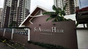 A sign for Sri Angsana Hillr condominium with a modern design and a view of surrounding high-rise buildings.