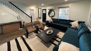 A modern living room with a staircase, dark blue sofa, wicker chairs, and a coffee table. - 112 S Washington Avenue (Lewes)