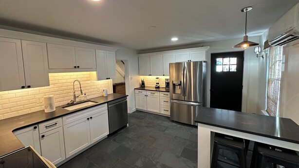 A modern kitchen with white cabinets, a stainless steel refrigerator, and a black countertop. - 112 S Washington Avenue (Lewes)