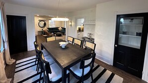 A dining area with a wooden table and chairs, a chandelier, and a kitchen in the background. - 112 S Washington Avenue (Lewes)